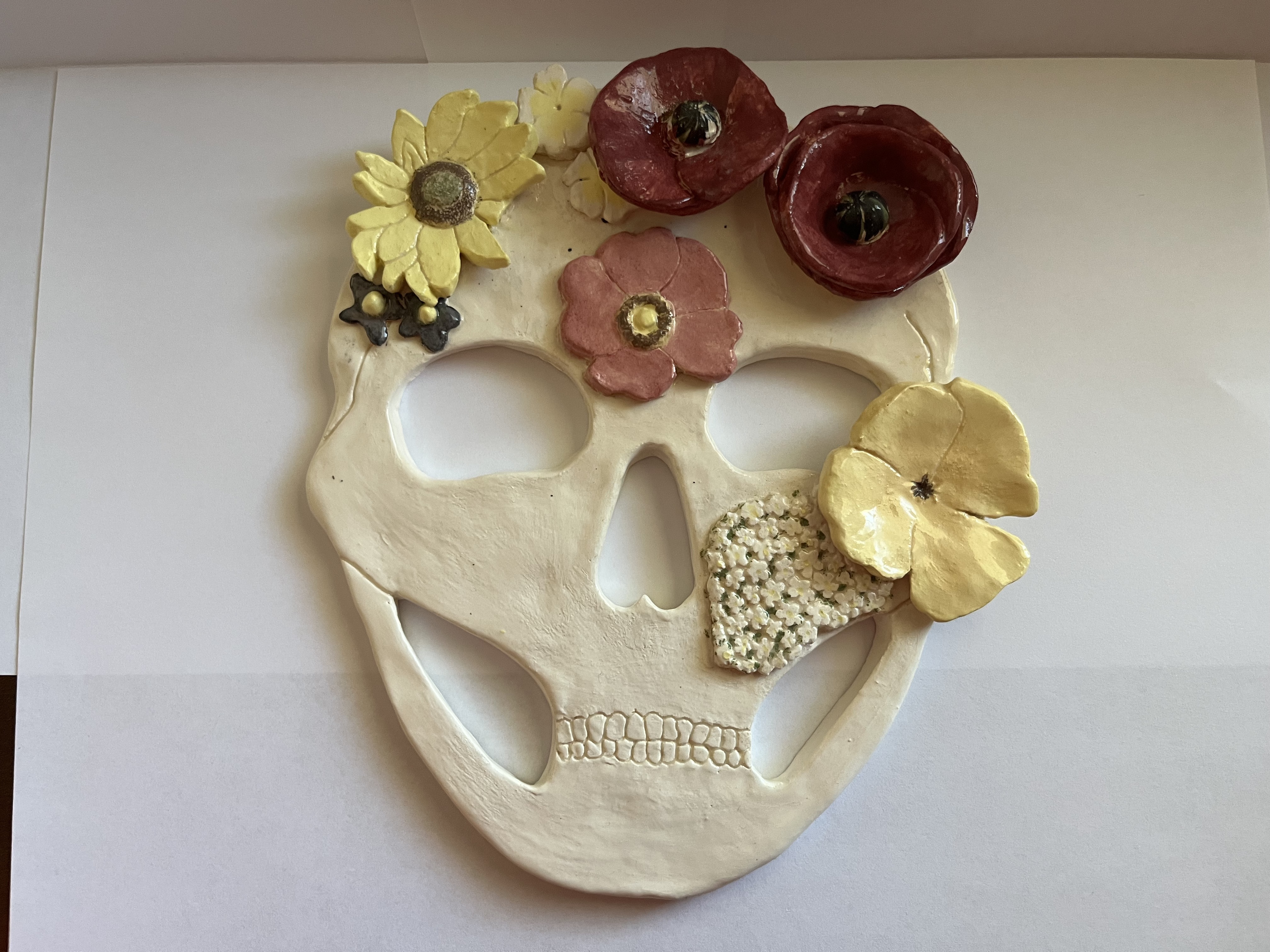 A flat ceramic mask of a human skull covered in various flowers
